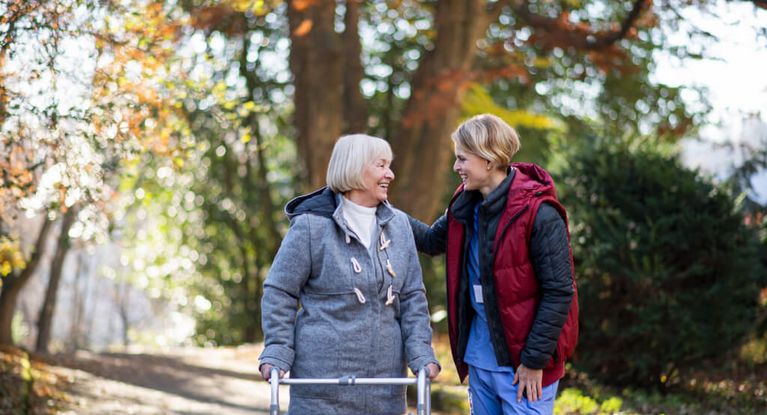 Pflegerin geht mit Senioren draußen im Herbst spazieren