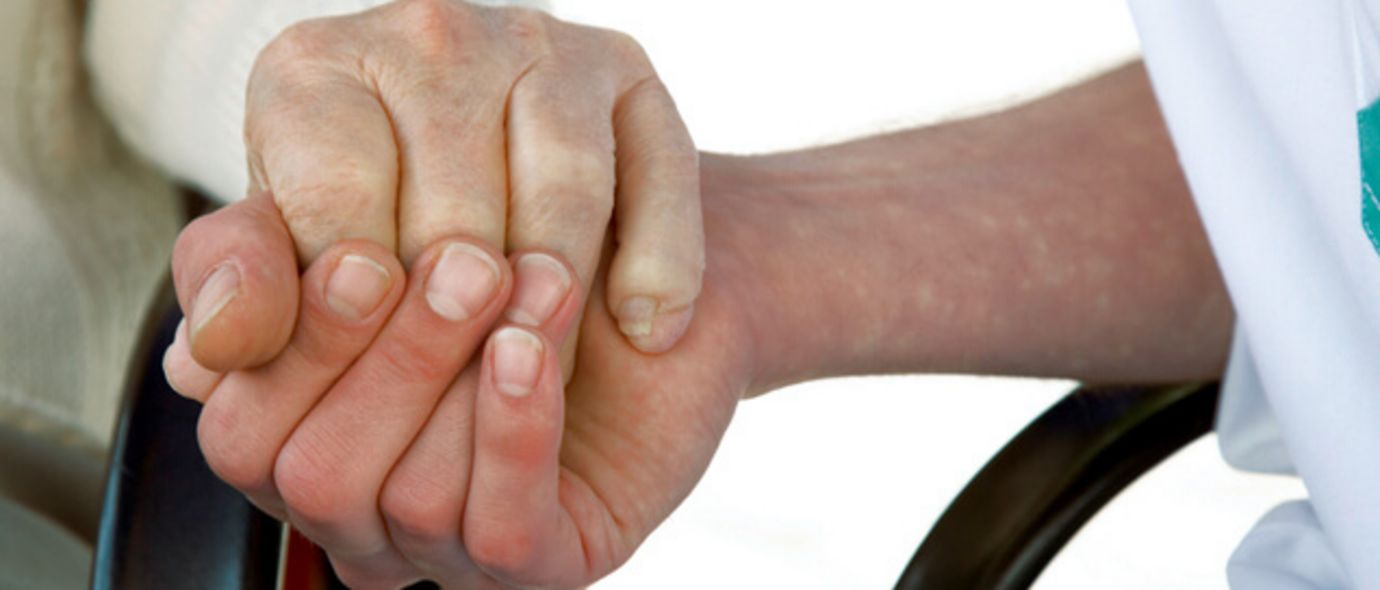 Pflegerin hält Hand einer Seniorin