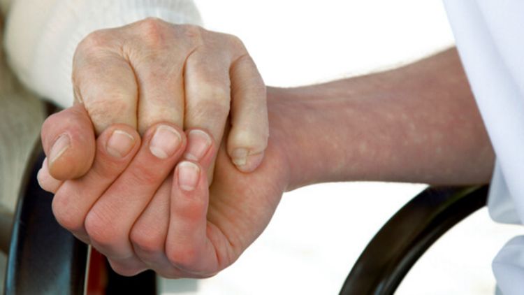 Pflegerin hält Hand einer Seniorin