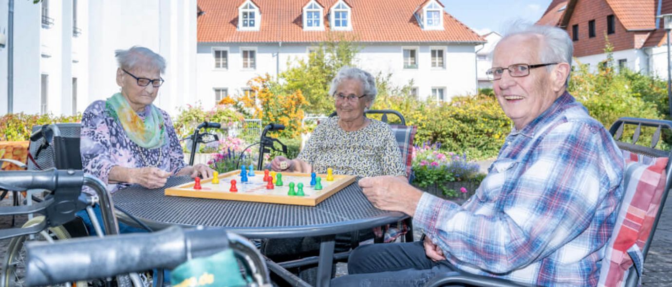 Senioren sitzen an einem Tisch draußen auf der Terrasse und spielen Mensch ärgere dich nicht