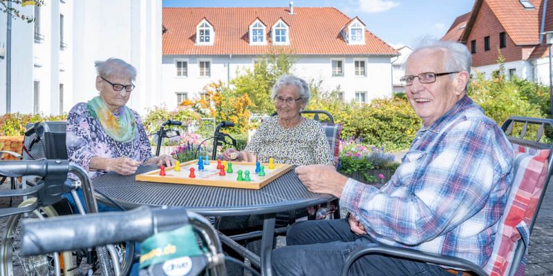 Senioren sitzen an einem Tisch draußen auf der Terrasse und spielen Mensch ärgere dich nicht