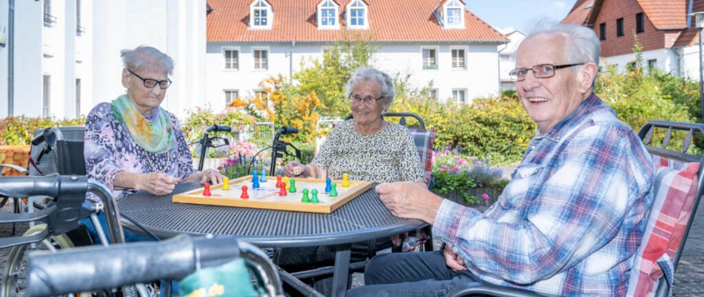 Senioren sitzen an einem Tisch draußen auf der Terrasse und spielen Mensch ärgere dich nicht