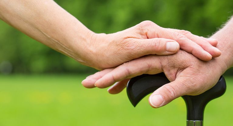 junge Hand liegt auf einer alten Hand, die sich auf einen Stock sützt
