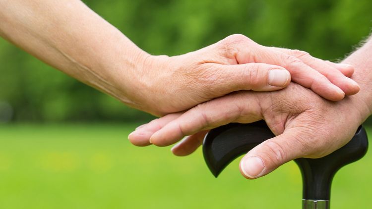 junge Hand liegt auf einer alten Hand, die sich auf einen Stock sützt