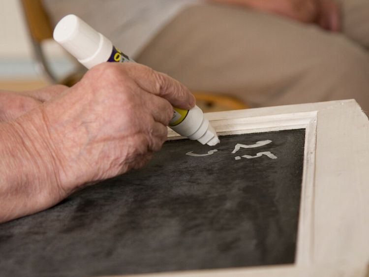 Seniorin schreibt mit Kreide auf eine schwarze Schiefertafel