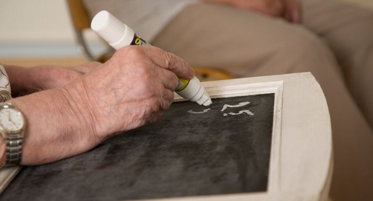 Seniorin schreibt mit Kreide auf eine schwarze Schiefertafel