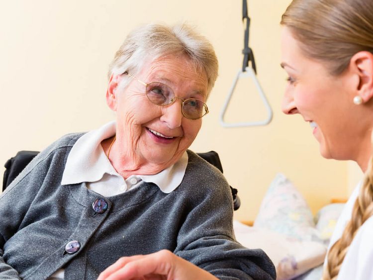 Pflegekraft behandelt die Hand einer älteren Person und beide lächeln sich an.