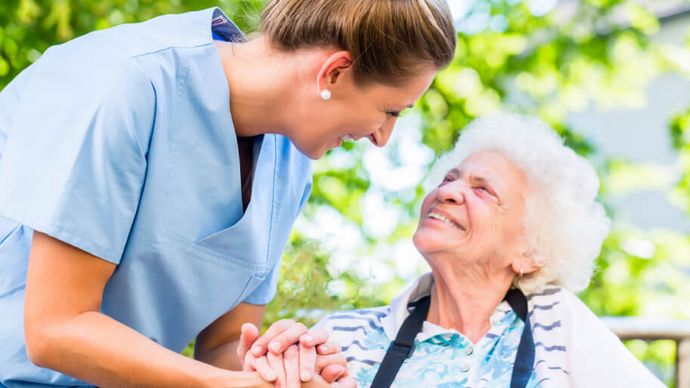 Altenpflegerin hält die Hand einer lächelnden Seniorin im Rollstuhl